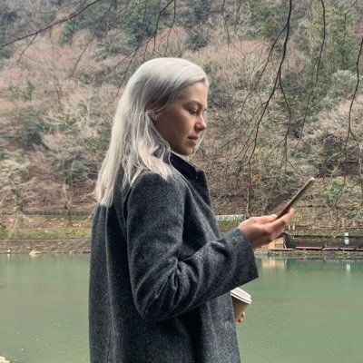 a picture of a blonde, white woman wearing a black coat and looking at her phone. presumably phoebe bridgers